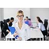Successful business woman standing with her staff in background at modern bright office