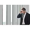 young business man talk by cellphone over bright window in big hall 