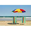 Beach chairs and umbrella on the ocean shore with surf in the background, horisontal