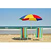 Beach chairs and umbrella on the ocean shore with surf in the background, horisontal