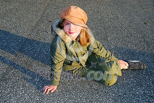 Young girl in a hat sitting on pavement, evening sun Young girl in a hat sitting on pavement, evening sun