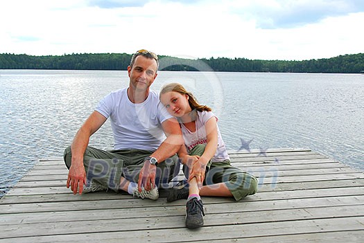 Father and child sitting on a wooden pier on a lake in nothern Ontrario Father and child sitting on a wooden pier on a lake in nothern Ontrario