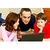 Father and children lying on the floor at home and looking into a portable computer