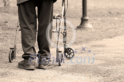 Senior man taking a walk in a park with the aid of a walking frame Senior man taking a walk in a park with the aid of a walking frame