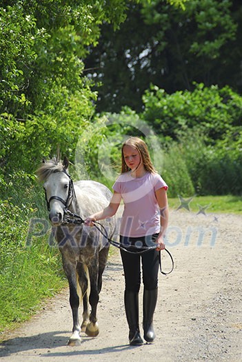 Young girl walking with a pony on a farm road Young girl walking with a pony on a farm road