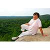 Mature woman sitting on scenic cliff edge smiling