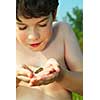 Young boy holding a tiny green frog in his hands