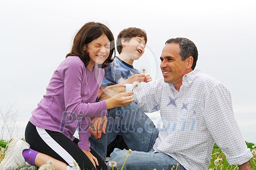 Children playing with their father blowing dandelions and laughing Children playing with their father blowing dandelions and laughing