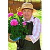 Senior woman holding a pot with flowers in her garden