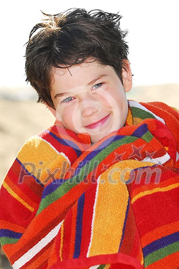 Young boy wrapped in a towel on a beach relaxing after swimming Young boy wrapped in a towel on a beach relaxing after swimming