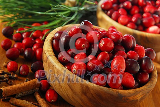 Fresh red cranberries in wooden bowls with spices and pine branches Fresh red cranberries in wooden bowls with spices and pine branches