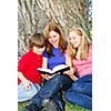 Family of mother and children reading a book under a tree in summer park