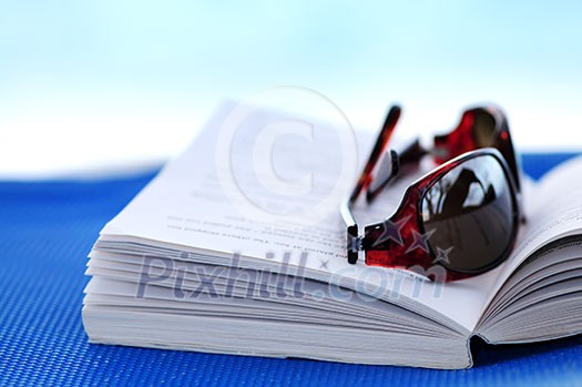 Sunglasses and open book on beach chair - summer vacation concept Sunglasses and open book on beach chair - summer vacation concept
