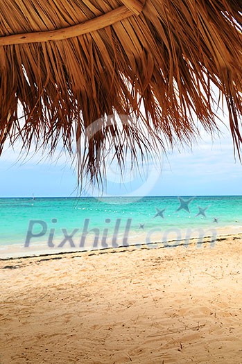 View from under palm leaves shelter onto tropical beach of a Caribbean island View from under palm leaves shelter onto tropical beach of a Caribbean island