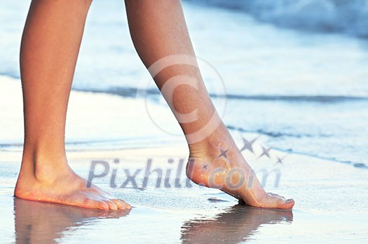 Feet of a young woman touching water on tropical beach Feet of a young woman touching water on tropical beach
