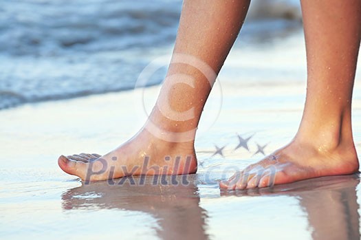 Feet of a young woman touching water on tropical beach Feet of a young woman touching water on tropical beach