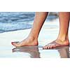 Feet of a young woman touching water on tropical beach