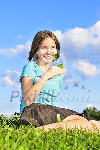 Young teenage girl sitting on grass and smelling a flower Young teenage girl sitting on grass and smelling a flower