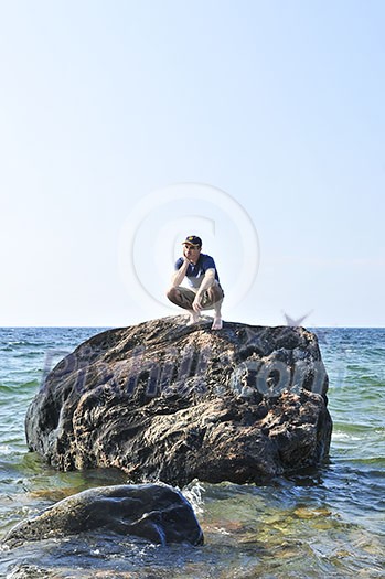 Man stranded on a rock in ocean waiting for rescue