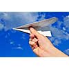 Child's hand holding a paper airplane on blue sky background