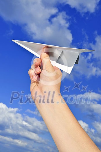 Child's hand holding a paper airplane on blue sky background Child's hand holding a paper airplane on blue sky background
