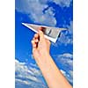 Child's hand holding a paper airplane on blue sky background