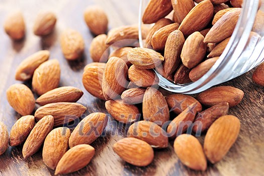 Raw almonds spilling out of small glass bowl Raw almonds spilling out of small glass bowl