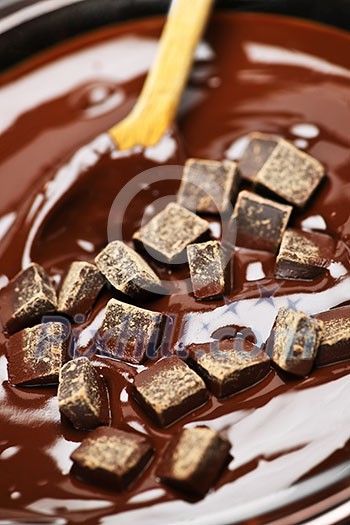 Wooden spoon stirring melting rich chocolate chunks Wooden spoon stirring melting rich chocolate chunks