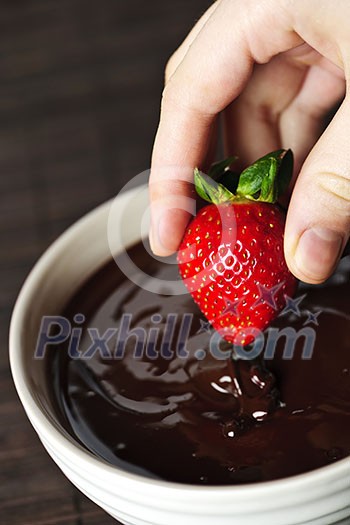 Hand dipping fresh strawberry in melted chocolate Hand dipping fresh strawberry in melted chocolate