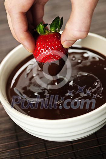 Hand dipping fresh strawberry in melted chocolate Hand dipping fresh strawberry in melted chocolate