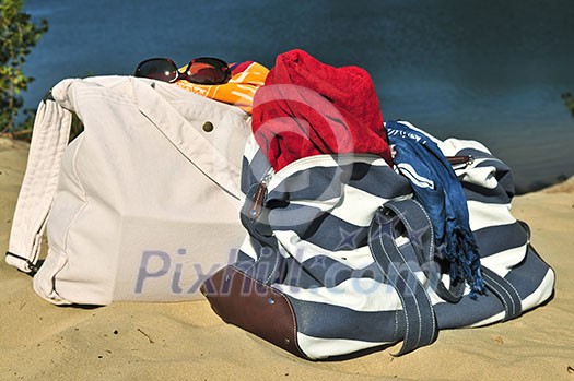 Summer beach bags on sand with towels and sunglasses Summer beach bags on sand with towels and sunglasses