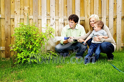 Happy family in backyard watering plant with hose Happy family in backyard watering plant with hose