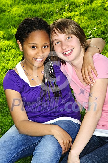 Two teenage girls sitting on grass and hugging Two teenage girls sitting on grass and hugging