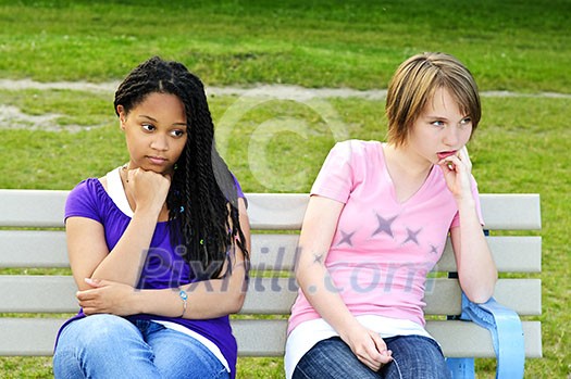 Two bored teenage girls sitting on bench Two bored teenage girls sitting on bench