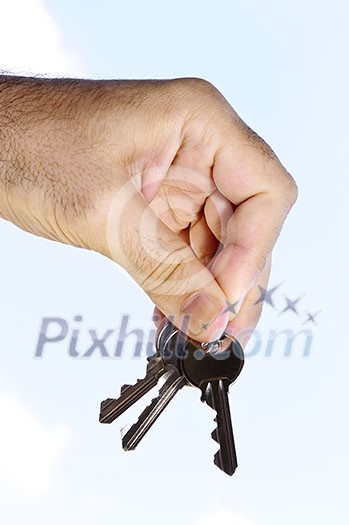 Man's hand holding house keys on blue sky background Man's hand holding house keys on blue sky background