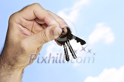 Man's hand holding house keys on blue sky background Man's hand holding house keys on blue sky background