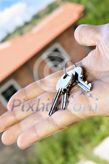 Man's hand holding keys with a house under construction in background Man's hand holding keys with a house under construction in background