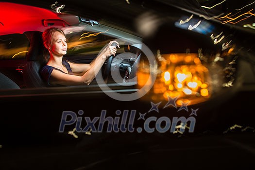 Driving a car at night - pretty, young woman driving her modern car at night, in a city (shallow DOF; color toned image)