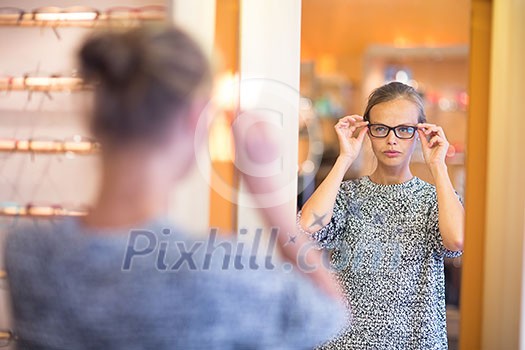 Pretty, young woman choosing new glasses frames in an optician store (color toned image; shallow DOF) Pretty, young woman choosing new glasses frames in an optician store (color toned image; shallow DOF)