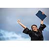 Pretty, young woman celebrating joyfully her graduation - spreading wide her arms, holding her diploma, savouring her success (color toned image; shallow DOF)