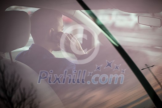 Handsome young man looking at his cellphone while at the wheel of his car, smiling Handsome young man looking at his cellphone while at the wheel of his car, smiling