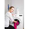 Housework: young woman doing laundry - putting colorful garments into the washing machine (shallow DOF; color toned image)