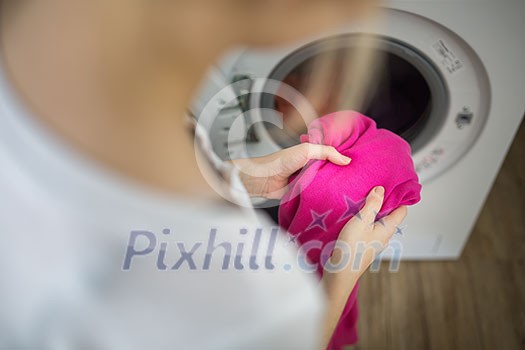 Housework: young woman doing laundry - putting colorful garments into the washing machine (shallow DOF; color toned image) Housework: young woman doing laundry - putting colorful garments into the washing machine (shallow DOF; color toned image)