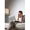 Very tired young woman, burning the midnigh oil - working late at night on her laptop computer, at home, sitting on sofa, rubbing her tired eyes, trying to stay focused