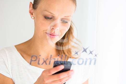 Pretty, young woman calling on her call phone, pensive, concentrating, wearing bright clothes inside a modern, fresh interior (color toned image; shallow DOF)
