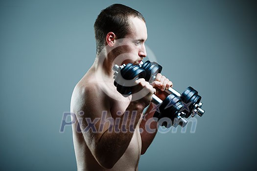 Close up of young man lifting weights over grey background (color toned image) Close up of young man lifting weights over grey background (color toned image)
