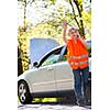 Young female driver wearing a high visibility vest, calling the roadside service/assistance after her car has broken down