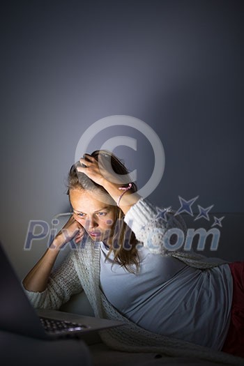 Very tired young woman, burning the midnigh oil - working late at night on her laptop computer, at home, sitting on sofa, trying to stay focused despite the fatigue Very tired young woman, burning the midnigh oil - working late at night on her laptop computer, at home, sitting on sofa, trying to stay focused despite the fatigue