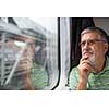Senior man enjoying a train travel - leaving his car at home, he savours the time spent travelling, looks out of the window, has time to admire the landscape passing by