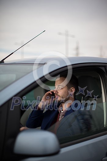 Handsome young man calling on his cellphone while at the wheel of his car Handsome young man calling on his cellphone while at the wheel of his car